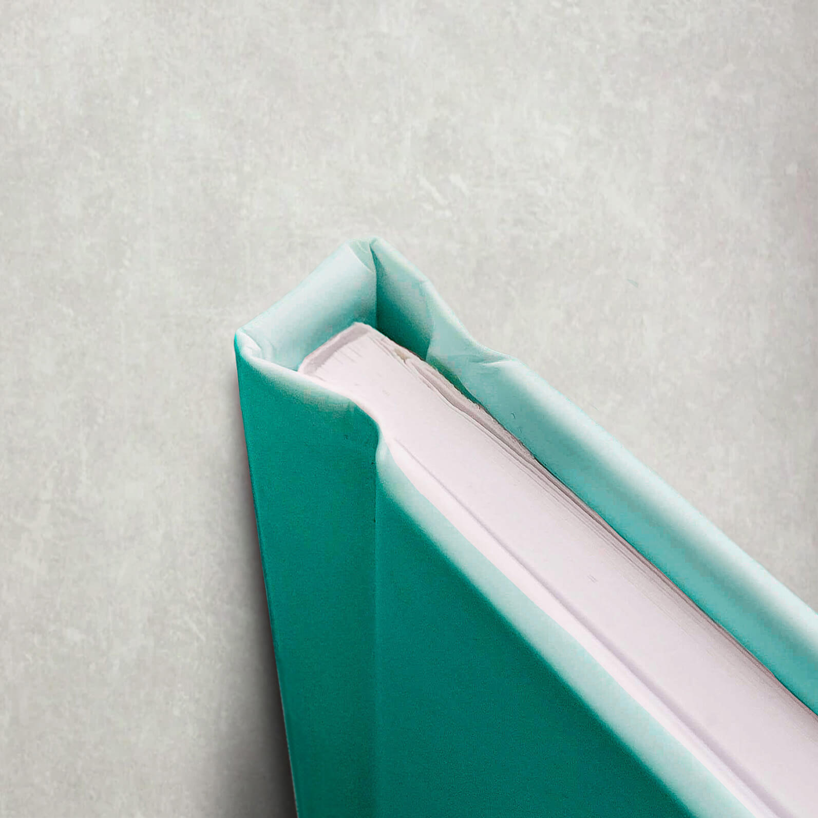 A close-up of a hardcover book with a green cover resting on a white surface, showcasing its casebound binding.