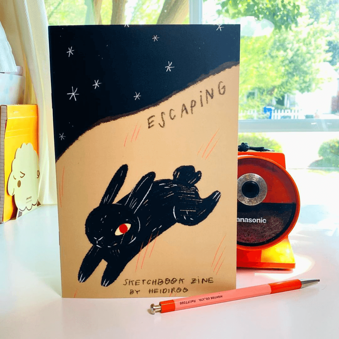 An upright zine print on a desk featuring an illustrated rabbit with a red eye.